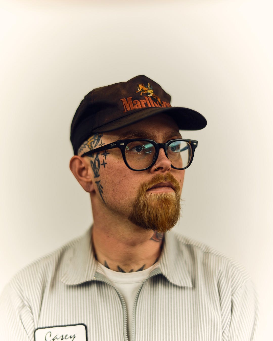 Casey Hart, white man, wearing a hat, and glasses looking 3/4 to the left.